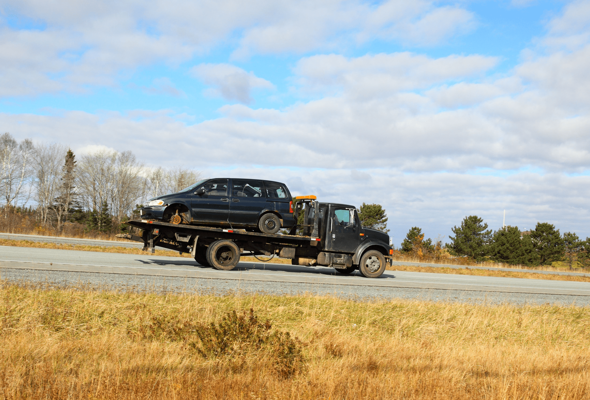 A tow truck carrying a black pickup truck on a highway.