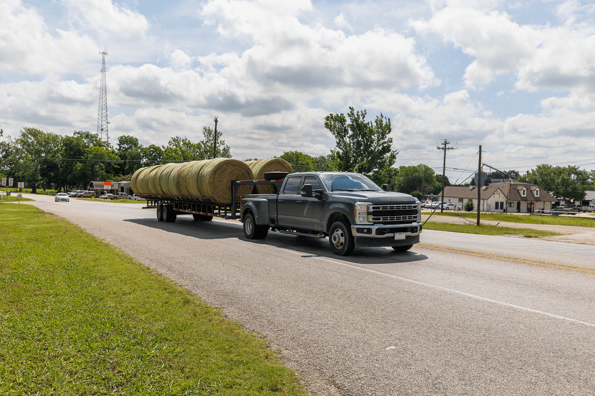 A truck hauling large cylindrical hay bales on a sunny road.