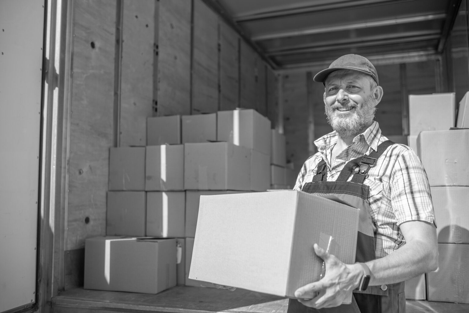 Smiling man holding a cardboard box in a storage area with stacked boxes.