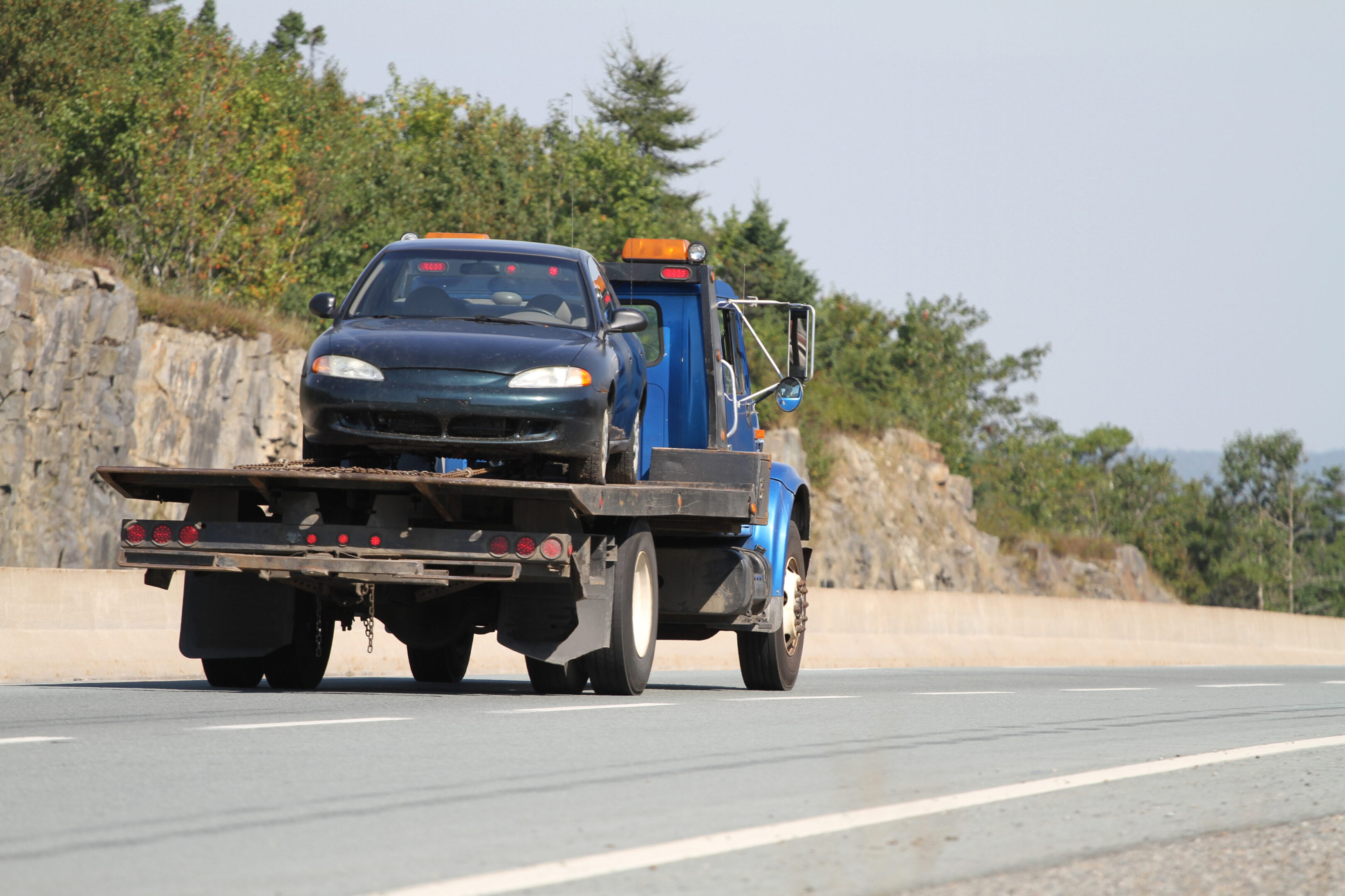 A car being towed on a flatbed tow truck on a road.